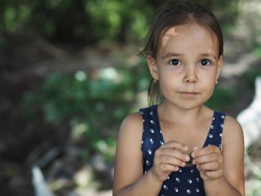 Kırsaldaki yeşil ağaçların arka planında bir ağaç yaprağı tutan küçük bir kız. Yaz günü.