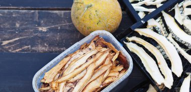 Sonbahar meyveleri tarım geçmişi. Bir kavun, ev kurutma makinesinden çıkan koyu renkte ızgaralarda kurutulmak için koyu bir arka plana serilir. Kavunları dilimlerle kurutuyoruz..