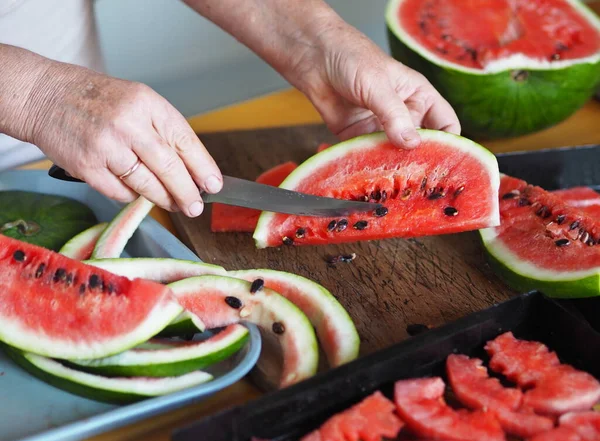 Yaşlı bir kadının elleri kuruması için bir karpuzu dilimlere ayırdı. Sonbahar meyveleri ve meyveleri. Tarım geçmişi ve karpuzlar. Kurutulmuş meyve toplama mevsimi.