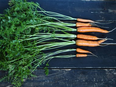 Kaba, koyu ahşap arka planda yeşil tepeli taze havuçlar. Yukarıdan görüntüle.