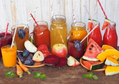 Çeşitli taze meyveler ve beyaz ahşap arka planlı ahşap bir masada farklı renklerde yeni hazırlanmış kokteyller. Kırsal biçim.