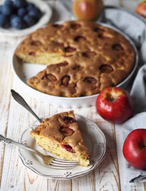 Gri arka planda beyaz seramik şeklinde elma ve erikli taze pişmiş yaz turtası. Ön planda dilimlenmiş kek. Gıda arkaplanı.