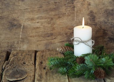 Noel 'de yanan bir mum, köknar dalları, tahta bir arka planda çam kozalakları. Metnin için bir yer. Tebrik kartı.