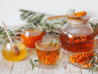 Cam bardakta vitamin dolu deniz dikenli çay çaydanlık, bal, reçel, taze çiğ deniz dikenli üzümleri ve beyaz mutfak masasında filizler. Deniz dikenli üzüm toplama mevsimi.