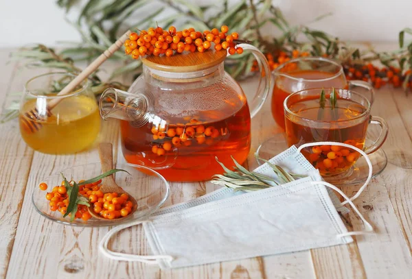 Yararlı deniz dikenli böğürtlenleri kullanılarak grip virüsünün korunması ve tedavi edilmesi kavramı. Deniz dikenli tıbbi maskeler bitkisel çay, reçel, bal ve deniz dikenli dallar beyaz arka planda böğürtlen.