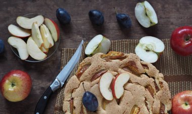 Ev yapımı elma ve erikli turta Charlotte yakın plan, ahşap arka planda elmalar ve mavi erikler..