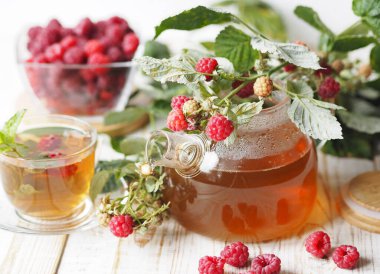 Sonbahar gecikmiş ahududu. Ahududulu tıbbi çayın faydalı özellikleri. Cam çaydanlıkta ahududulu bir dal ve hafif bir arka planda çay..