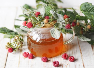Sonbahar gecikmiş ahududu. Ahududulu tıbbi çayın faydalı özellikleri. Cam çaydanlıkta ahududulu bir dal ve hafif bir arka planda çay..