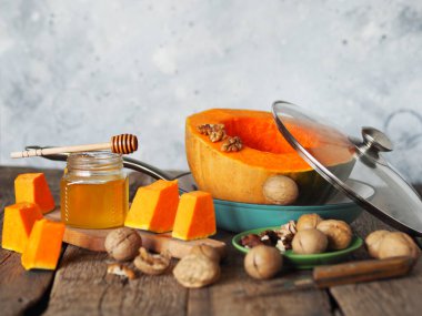 Kızartma tavasında dilimlenmiş portakal kabağı, ballı ve cevizli eski bir masa ve gri arka plan. Ev yemeği. Sonbahar arkaplanı.