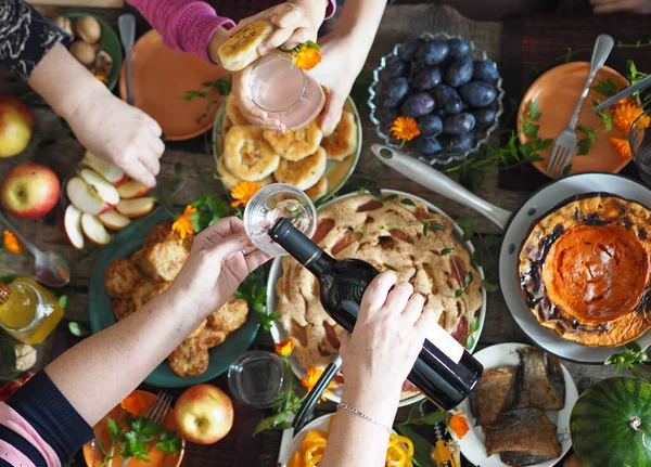 Concepto de celebración del Día de Acción de Gracias. Hay mucha comida en la mesa de madera.Los huéspedes vierten vino tinto y toman alimentos naturales caseros saludables con sus manos.. —  Fotos de Stock