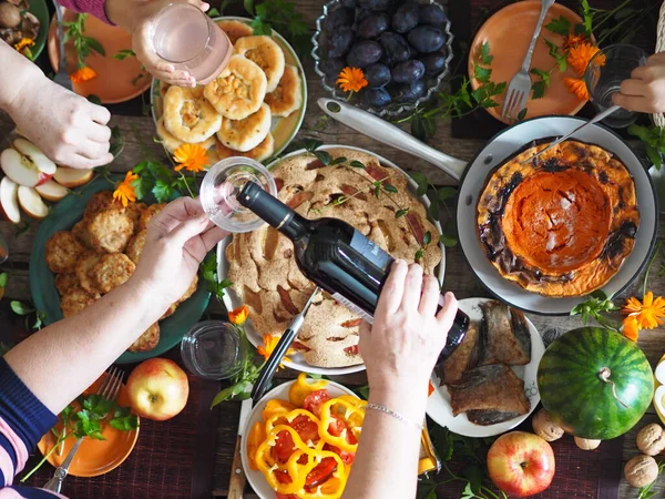 Concepto de celebración del Día de Acción de Gracias. Hay mucha comida en la mesa de madera.Los huéspedes vierten vino tinto y toman alimentos naturales caseros saludables con sus manos.. —  Fotos de Stock