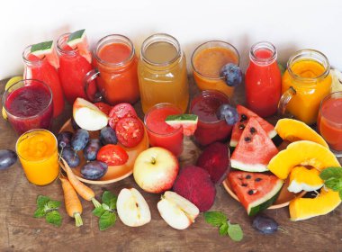 Taze meyve yığını ve ahşap bir masa üzerinde farklı renklerde yeni hazırlanmış kokteyller..