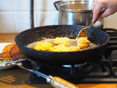 The process of frying natural dietary pumpkin and millet pancakes in a pan on the stove. An elderly woman's homemade food. Country style. clipart