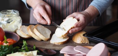 Ev yemeği. Yaşlı kadın arkadaşlarıyla tanışmaya hazırlanıyor ve peynirli, domatesli, kızarmış sosisli sandviç hazırlıyor. Sağlıklı doğal yiyecekler..