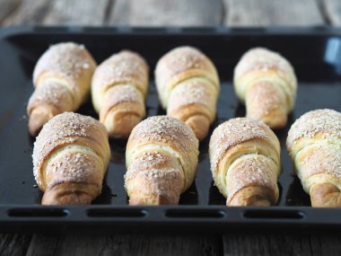 Eski ahşap bir arka planda, fırının tepsisine susam ve şeker serpiştirilmiş kruvasanlar. Ev yapımı kek..