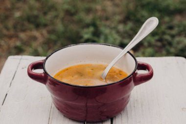 Kasabadaki yalnızlık sırasında doğada öğle yemeği. Ekşi kremalı bir tabak köy çorbası ve sokağın arka planında yeşil bulanık, tahta beyaz bir masada bir kaşık..