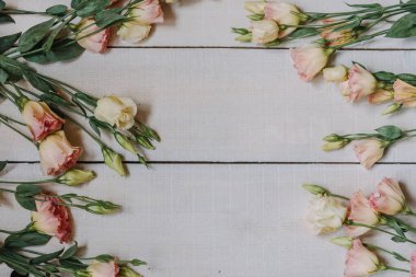Bir davetiye veya kartpostal için güzel sanatlar tarzında beyaz ve pembe övgü çiçeklerinden yapılmış bir çerçeve. Pastel renklerde metin ve kopyalama alanı olan beyaz tahta bir arkaplanda Eustoma çiçekleri.