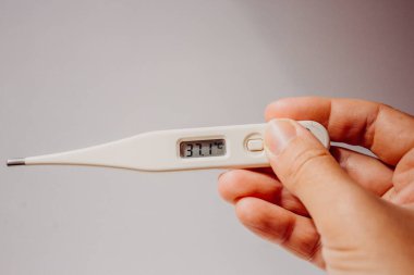 Hastalık ve ateş. Koronavirüsün ilk belirtileri. Elektronik termometre, elinde 37.1 derecelik bir ekran değeri olan açık beyaz arka planda, metin için yeri olan bir kadının elinde..