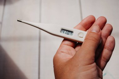 Hastalık ve ateş. Koronavirüsün ilk belirtileri. Elektronik termometre, elinde 41 derecelik bir ekran değeri olan açık beyaz arka planda metin için yeri olan bir kadının elinde..