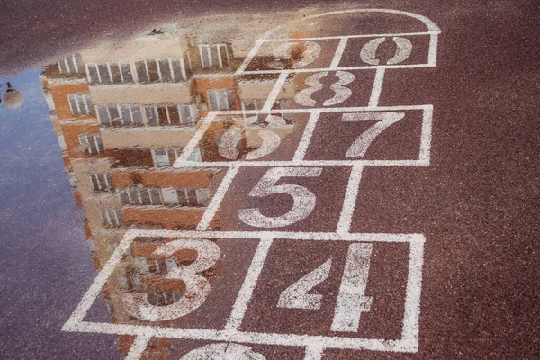 The concept of bad weather. Marking for popular children\'s games on the street in the yard on the sports surface after the rain with the reflection of a part of a multi-storey building in a puddle.