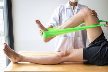 Doktor ya da fizyoterapist, yaralı erkek hasta bacağını tedavi ediyor, klinikte rehabilitasyon tedavisi uyguluyor..