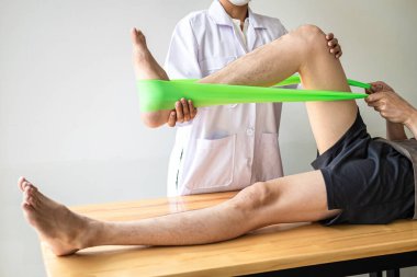 Doktor ya da fizyoterapist, yaralı erkek hasta bacağını tedavi ediyor, klinikte rehabilitasyon tedavisi uyguluyor..