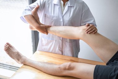 Doktor ya da fizyoterapist, yaralı erkek hasta bacağını tedavi ediyor, klinikte rehabilitasyon tedavisi uyguluyor..