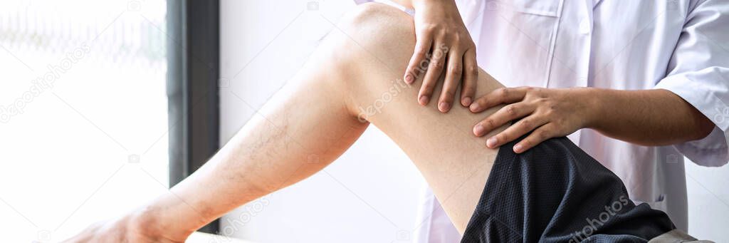 Doctor or Physiotherapist working examining treating injured leg of athlete male patient, Doing the Rehabilitation therapy pain in clinic.