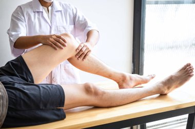 Doktor ya da fizyoterapist, yaralı erkek hasta bacağını tedavi ediyor, klinikte rehabilitasyon tedavisi uyguluyor..