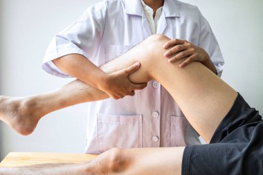 Kadın fizyoterapist, erkek hastanın yaralı bacağını tedavi ediyor, rehabilitasyon tedavisi uyguluyor, klinikte acı çekiyor..