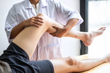 Kadın fizyoterapist, erkek hastanın yaralı bacağını tedavi ediyor, rehabilitasyon tedavisi uyguluyor, klinikte acı çekiyor..