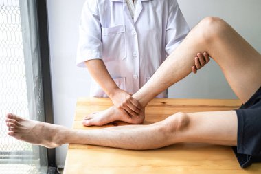 Doktor ya da fizyoterapist, yaralı erkek hasta bacağını tedavi ediyor, klinikte rehabilitasyon tedavisi uyguluyor..