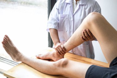 Kadın fizyoterapist, erkek hastanın yaralı bacağını tedavi ediyor, rehabilitasyon tedavisi uyguluyor, klinikte acı çekiyor..