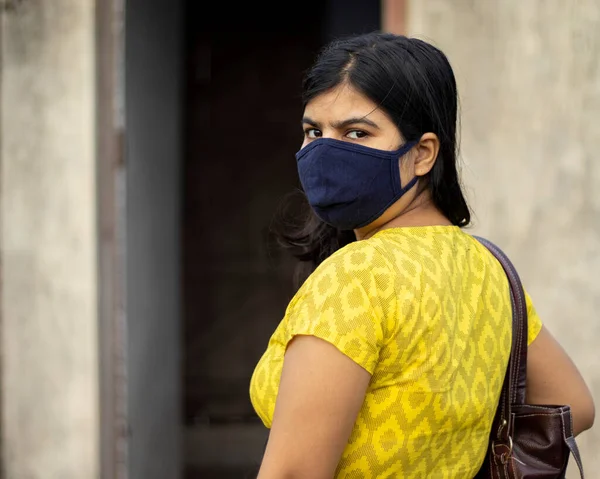 an Indian woman in yellow dress and face mask on is going outside with bag after unlock 1.0 of corona virus pandemic