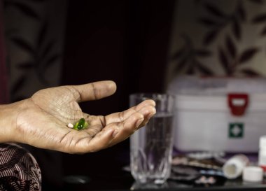 İnsan eliyle ilgili tablet ve kapsül seçici bir odak noktası, su bardağı ve evde kullanılan ilaçlar.