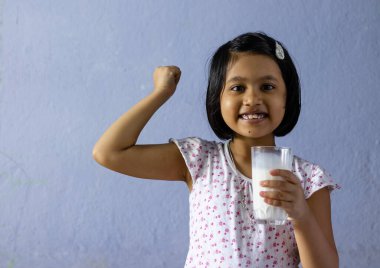 Küçük şirin Hintli / Asyalı kız elinde gülen yüzlü bir bardak süt tutuyor - sağlıklı beslenme konsepti
