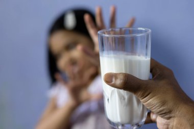 Hintli / Asyalı bir kıza verilen süt dolu bardağın seçici odağı onu içmek istemeyen