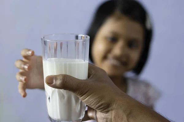 selective focus of a glass full of milk being given to a an Indian / Asian girl child who stretches hand with smiling face