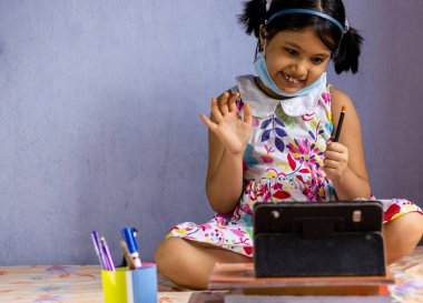 COVID-19 salgını sırasında online tablet derslerine gülen bir Hintli kız çocuğu katılıyor.