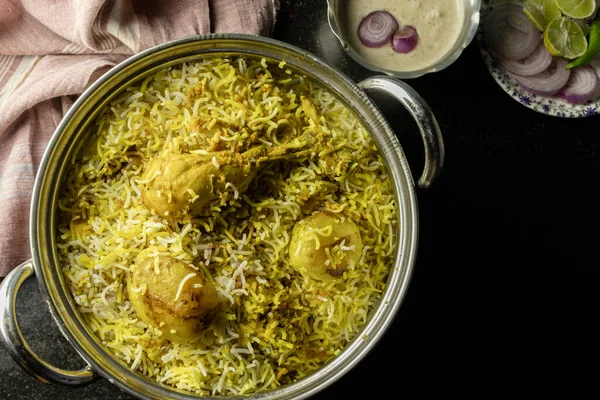 Lezzetli ve baharatlı ev yapımı tavuk biryani geleneksel kase içinde raita ve siyah arka planda salata.