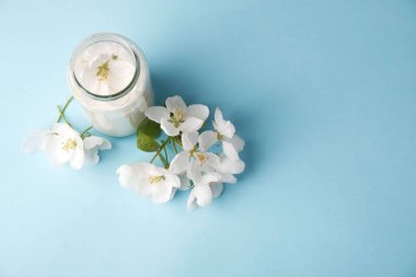 Mavi arkaplanda cam kavanozda elma ağacı çiçekleri, fotokopi alanı, doğal kozmetik konsepti, aromaterapi, bitkisel ilaç.