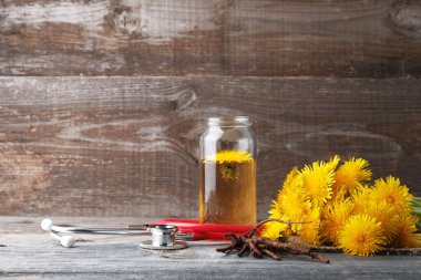 Cam kavanozda karahindiba suyu çorbası ve fotokopi alanı, şifalı bitkiler, bitkisel ilaçlar, doğal kozmetik, bitkisel konsept içeren eski ahşap zemin üzerinde steteskop.