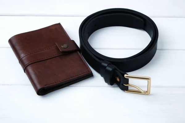 Wallet and belt made of genuine leather on white wooden background with copy space, handmade mens accessories.