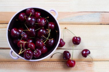 Tahta arka planda yuvarlak bir kasede kuyrukları olan kırmızı kirazlar. Üst görünüm, masadaki birkaç yalan. Metin için kopyalanma alanı