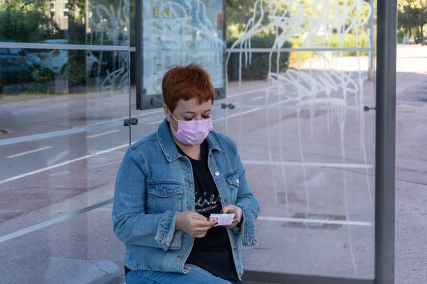 Attractive modern middle-aged woman with redhead virus mask Sitting waiting for the arrival of the bus