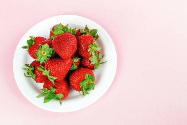 Pembe arka planda beyaz bir tabakta çilek, metin için yeri olan üst görünüm.