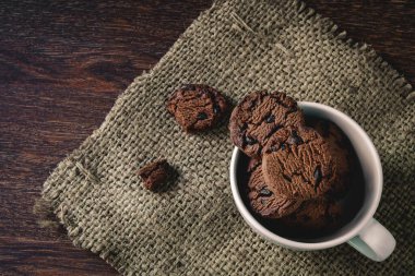 Tahta bir masada, fincanda çikolatalı kurabiye.