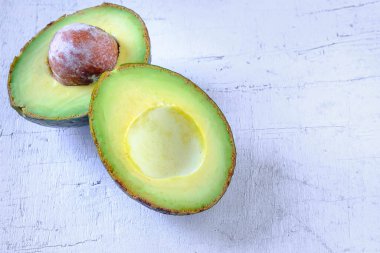 Avokado meyvesi beyaz ahşap bir masada ikiye bölünmüş..