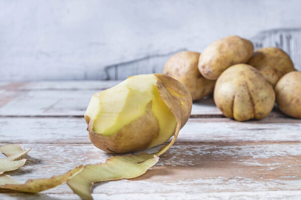 Potatoes are peeled on wooden background.