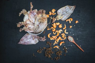 Kurutulmuş deniz ürünleri, kurutulmuş mürekkep balığı ve kurutulmuş karideslerle siyah ahşap bir masada.